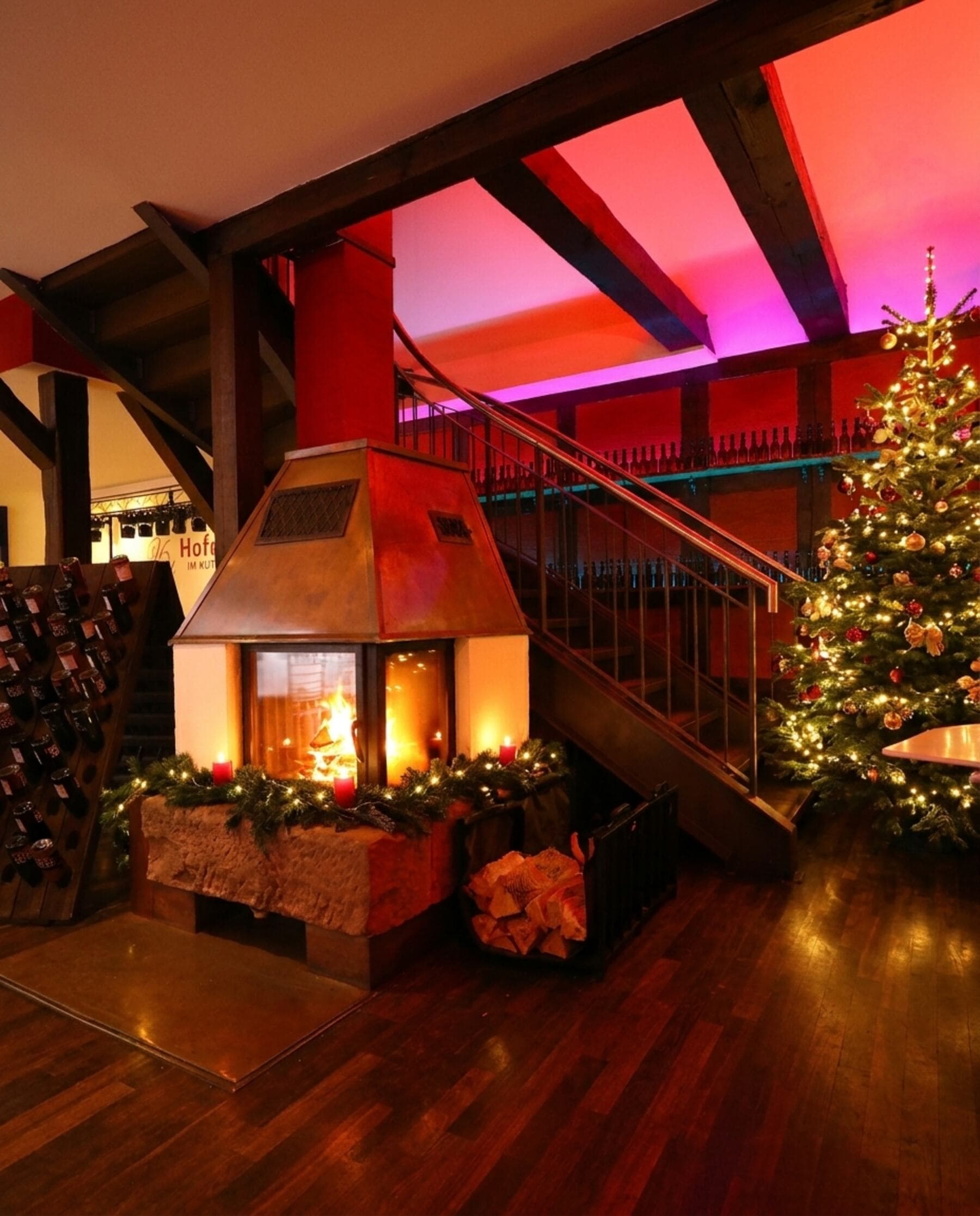 Der offene Kamin im Hofmeister mit brennendem Feuer, daneben ein geschmückter Weihnachtsbaum mit warmen Lichtern, auf dem Sims eine Tannengirlande und rote Kerzen