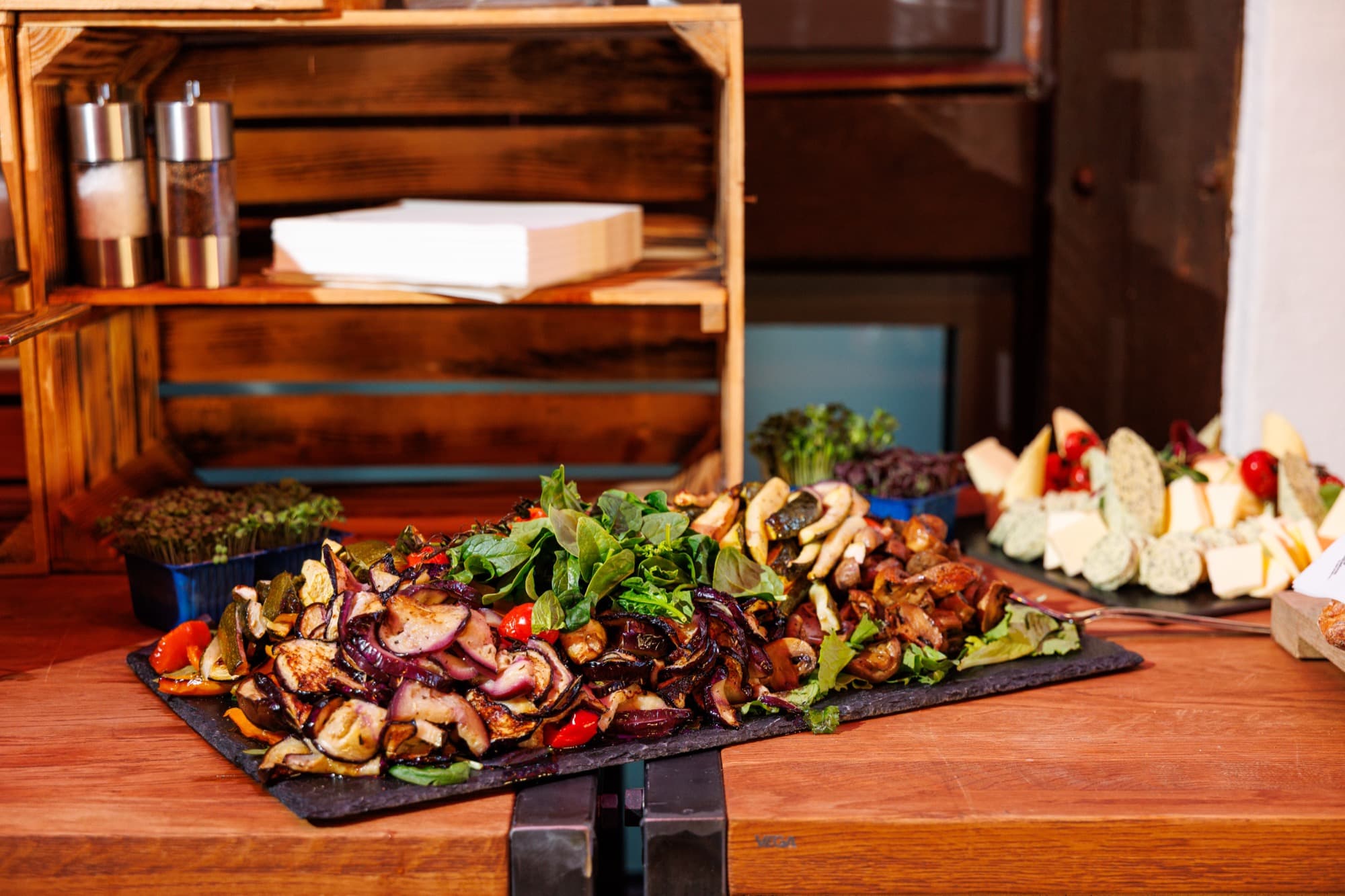 Schieferplatte mit gegrilltem Gemüse und Kräutersalat, daneben eine Käseplatte mit Trauben