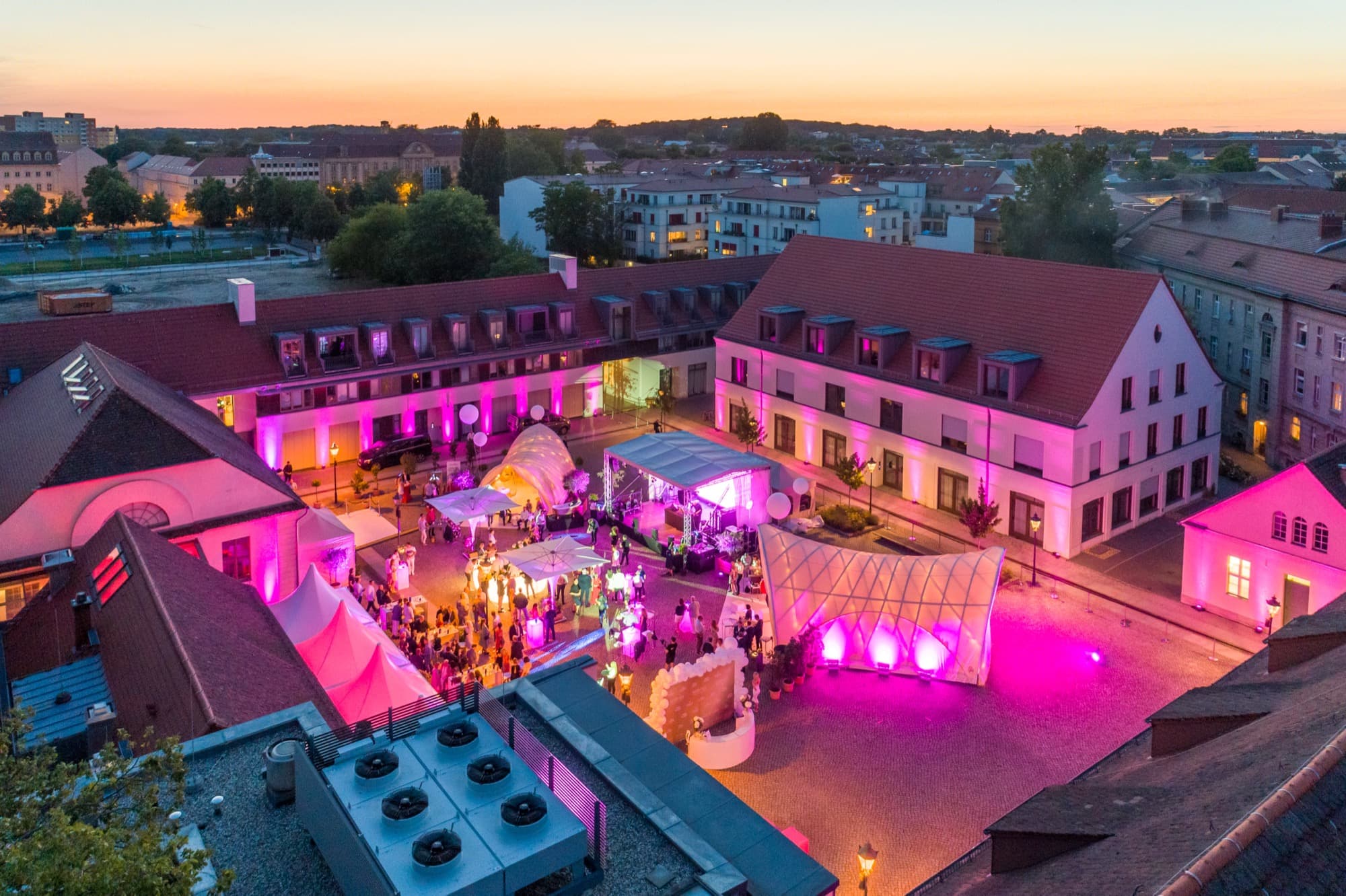 Der Innenhof aus der Luft zur blauen Stunde, die Gebäude in Pink angestrahlt, Zelte, Bühne und Gäste auf dem Pflaster