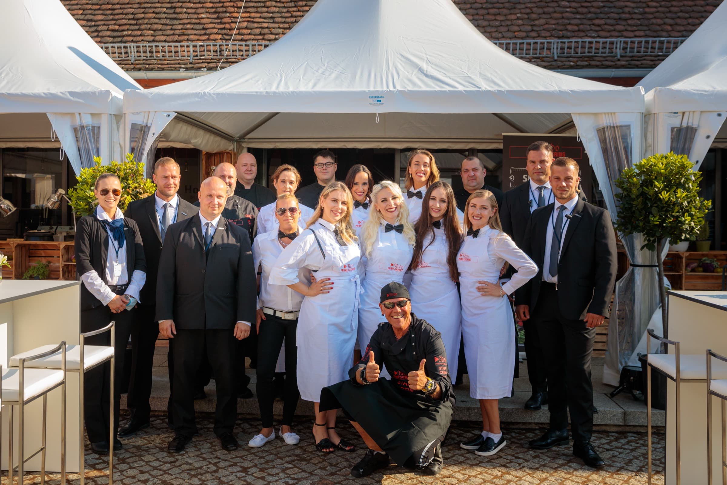 Das Team im Innenhof vor den weißen Zelten, Servicekräfte in weißen Schürzen und Kollegen im Anzug, vorne kniend der Geschäftsführer