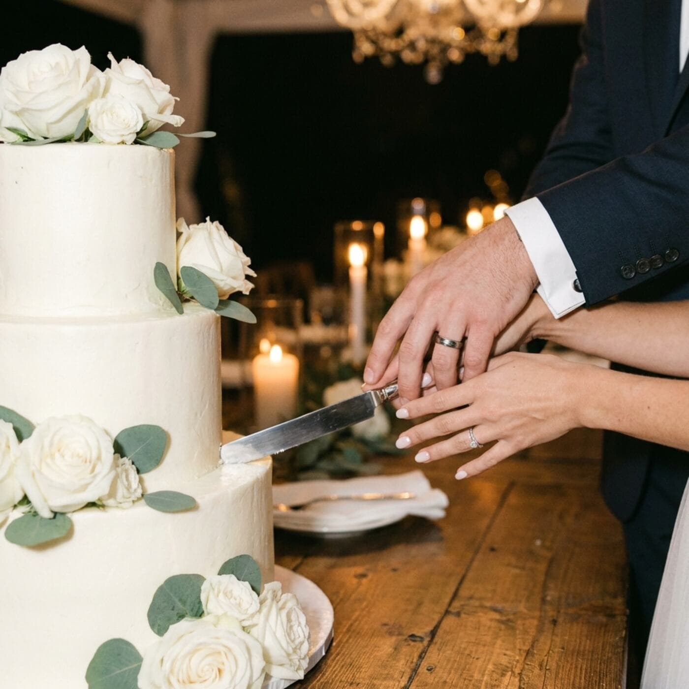 Das Brautpaar schneidet gemeinsam die weiße Hochzeitstorte an, zu sehen sind nur die Hände am Messer