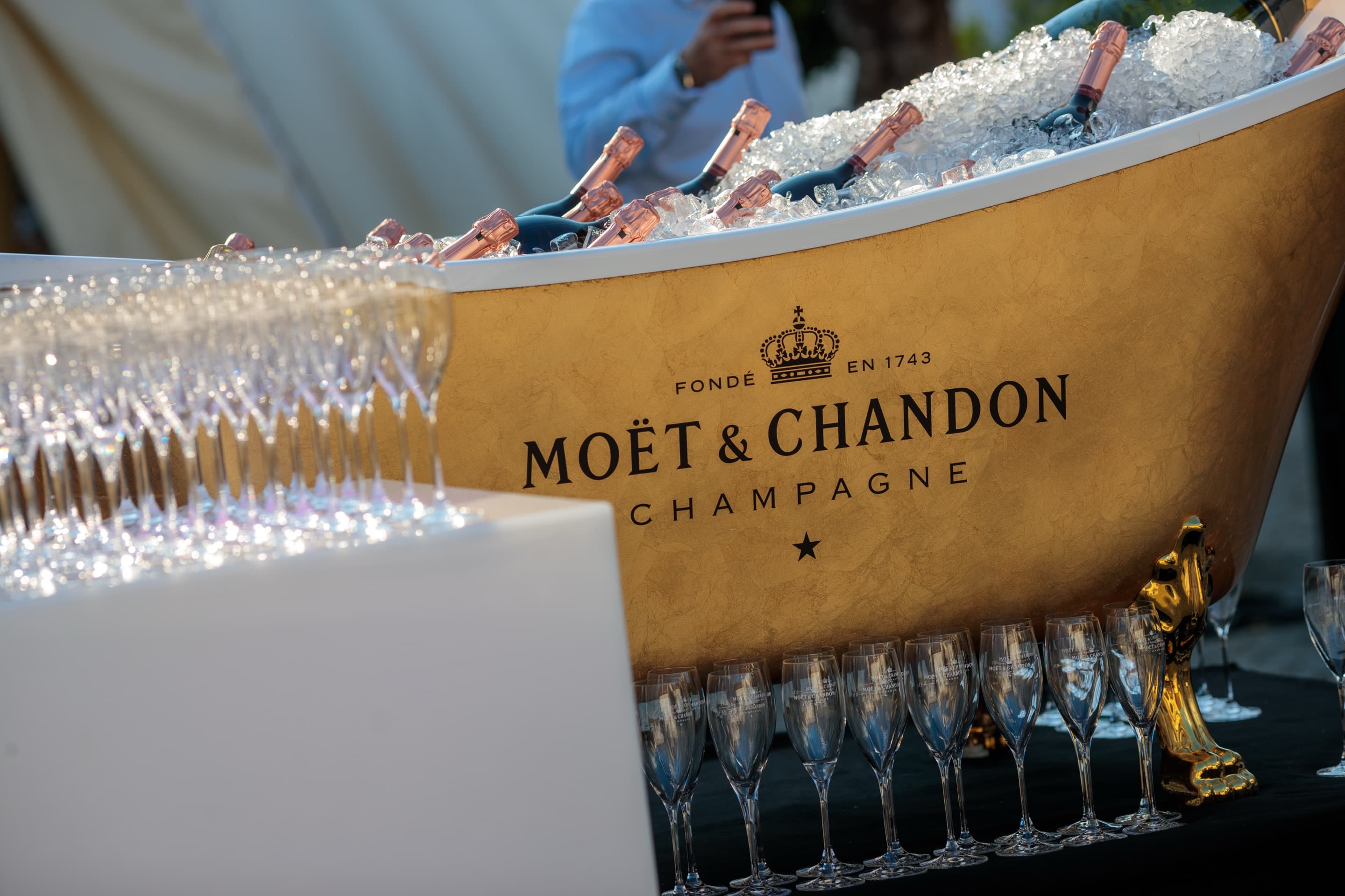 Goldene Wanne voller Eis mit gekühlten Champagnerflaschen, davor lange Reihen bereitstehender Sektgläser